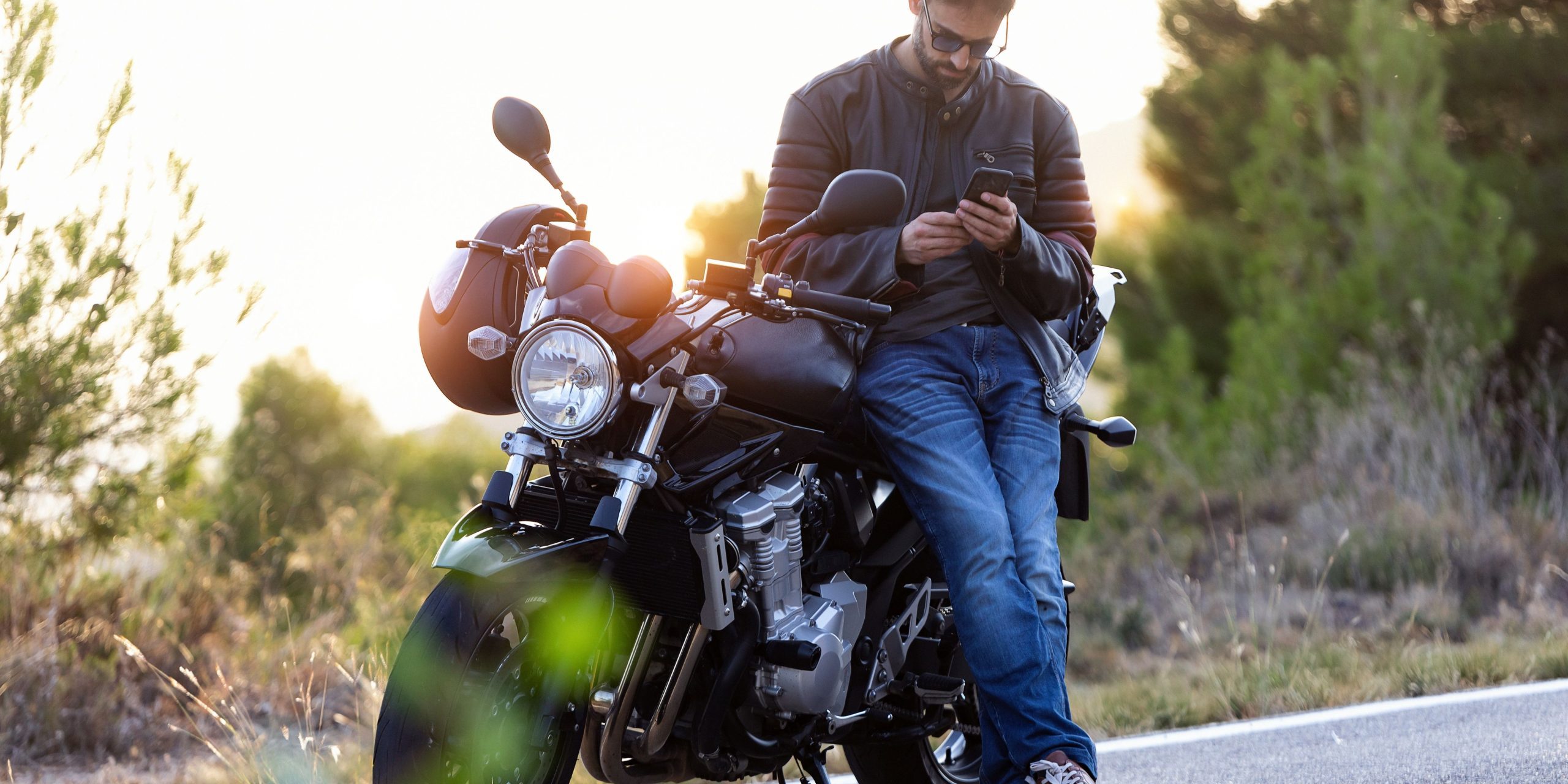 Man with motorcycle in Texas reviewing insurance coverage on his phone.